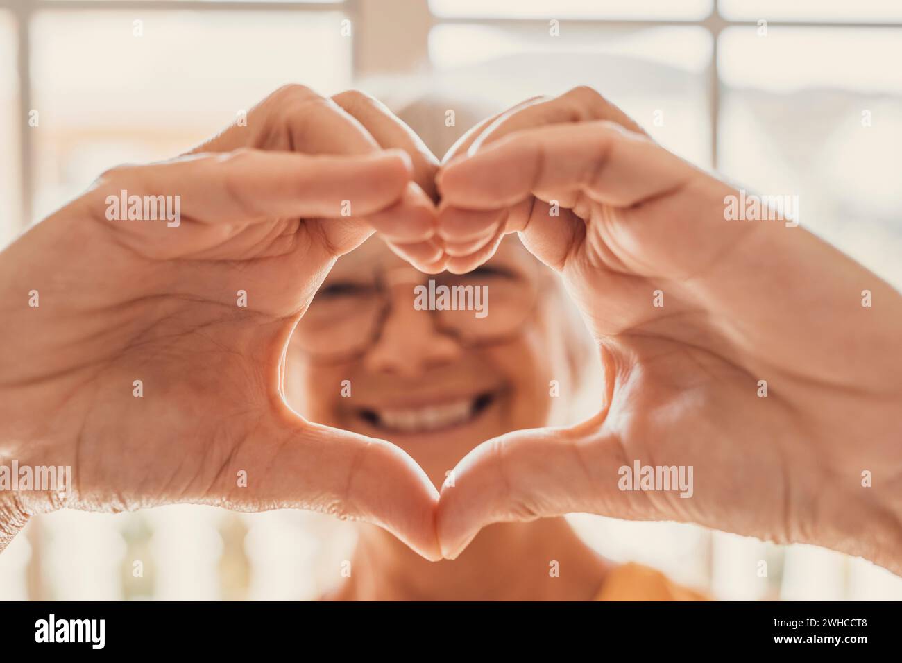 Ältere Frau sitzen im Wohnzimmer verbundene Finger zeigen Herzsymbol Nahaufnahme, alte Menschen Herz Herz-Kreislauf-Vorbeugung Behandlung, Gesundheitscheck, Herz-Kreislauf-Vitamine, Zeichen der Freundlichkeit und Wohltätigkeit Stockfoto