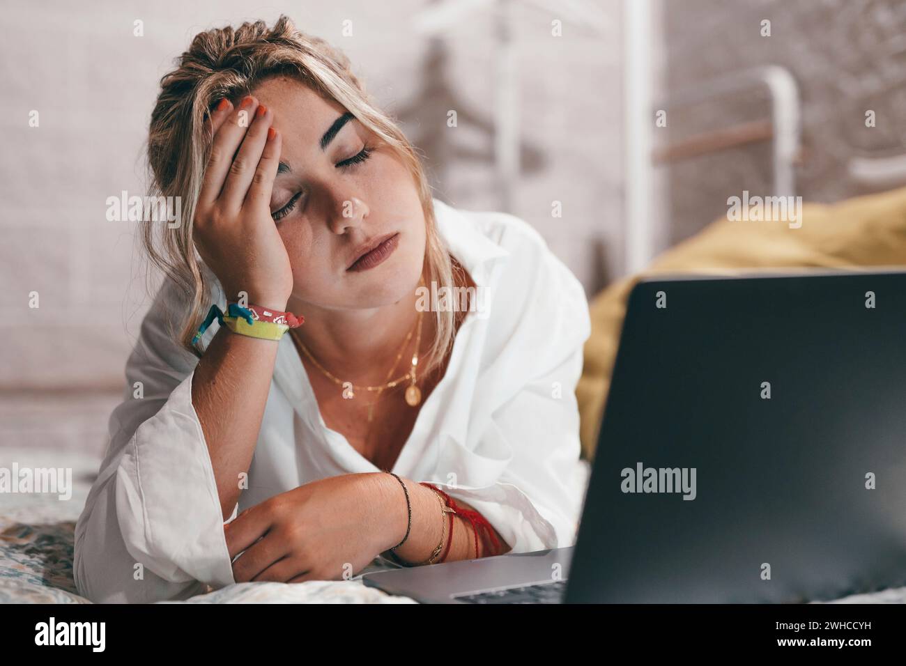 Nahaufnahme einer jungen Frau, die zu Hause im Schlafzimmer einen Laptop benutzte, schwere Kopfschmerzen hatte und sich nachts krank und erschöpft fühlte. Berühren Sie ihren Kopf massierend Stockfoto