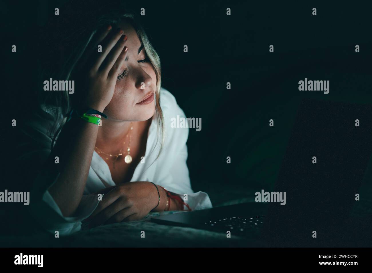 Überwältigter junger kaukasischer Student, der den Kopf berührt, unter verschwommenem Sehvermögen leidet, die Nasenbrücke massiert, die Schmerzen lindert, sich erschöpft fühlt, am späten Abend am Computer im Bett zu arbeiten. Stockfoto