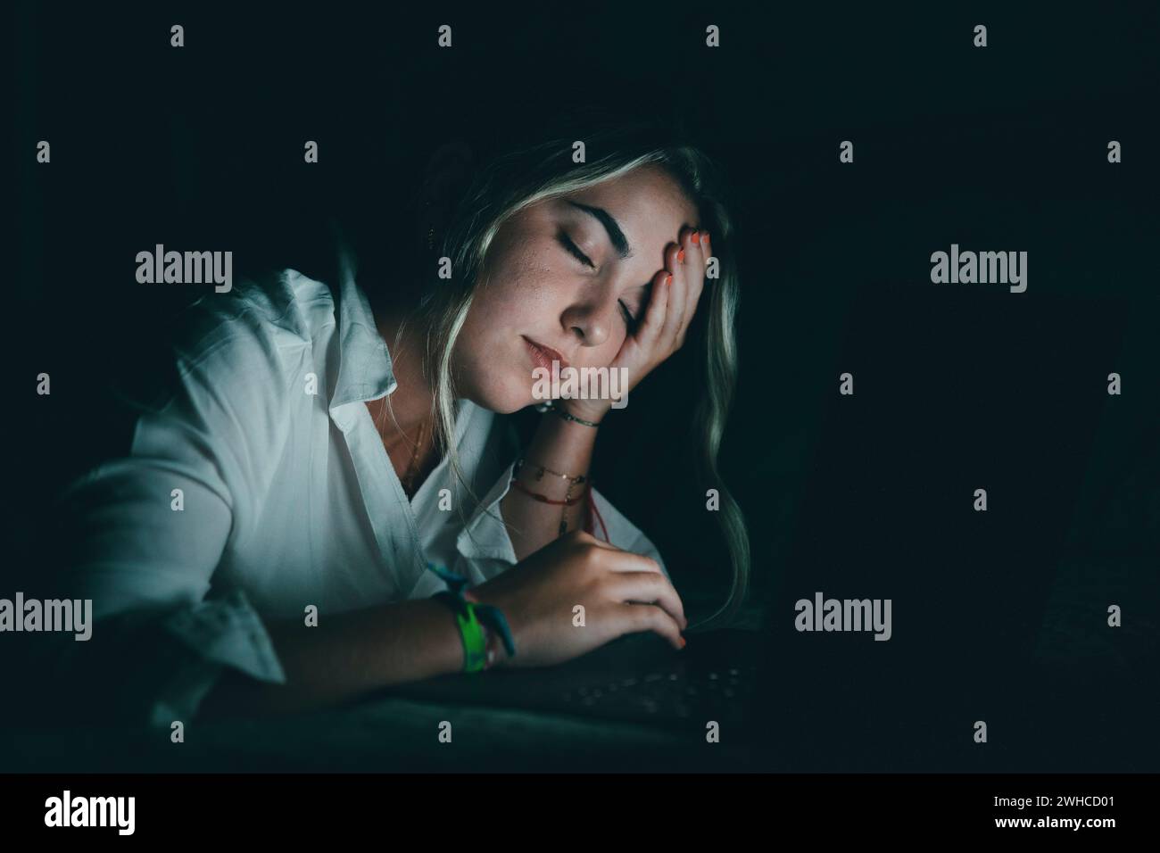 Überwältigter junger kaukasischer Student, der den Kopf berührt, unter verschwommenem Sehvermögen leidet, die Nasenbrücke massiert, die Schmerzen lindert, sich erschöpft fühlt, am späten Abend am Computer im Bett zu arbeiten. Stockfoto