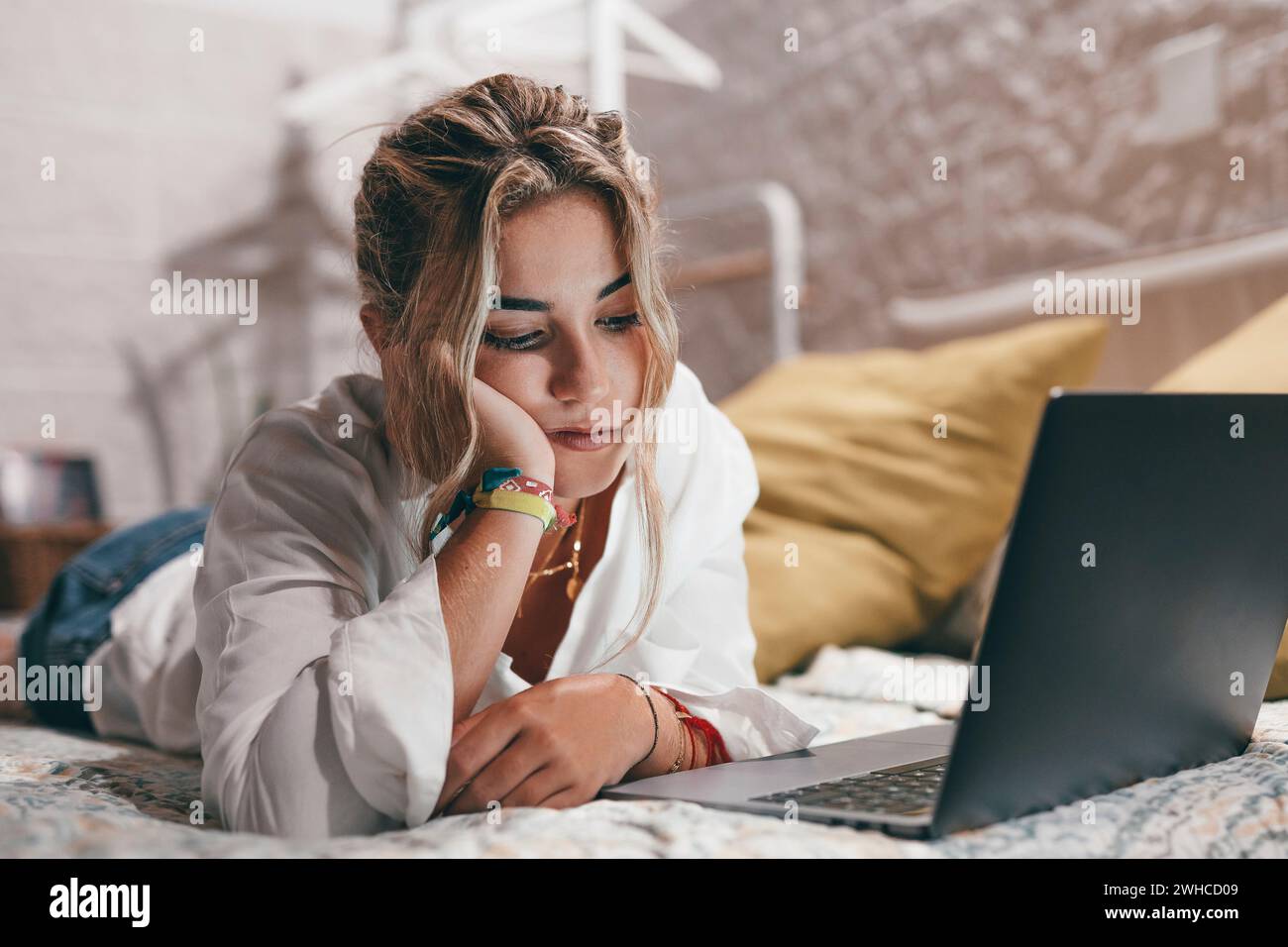 Nahaufnahme einer jungen gelangweilten Frau, die zu Hause einen Laptop benutzte, der auf dem Bett lag und im Netz surfte. Millennial müde weibliche Teenagerin, die online studiert. Stockfoto