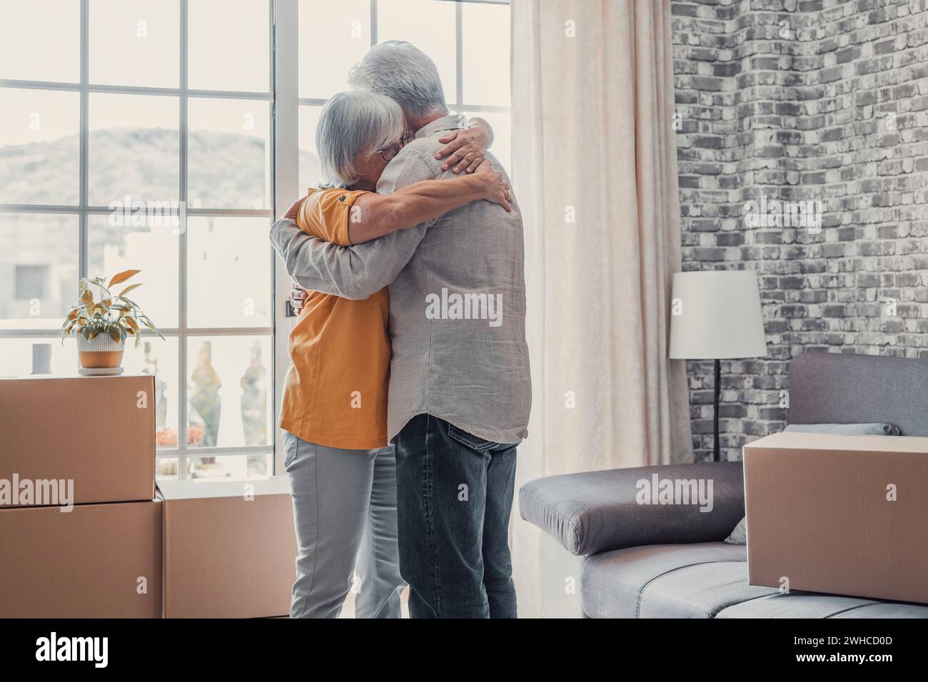 Glückliche dankbare ältere Frau, die Ehemann mit Liebe umschließt, Zuneigung in stapelbaren Kartons in der neuen Wohnung, feiert Immobilienkäufe, zieht in ein neues Zuhause Stockfoto