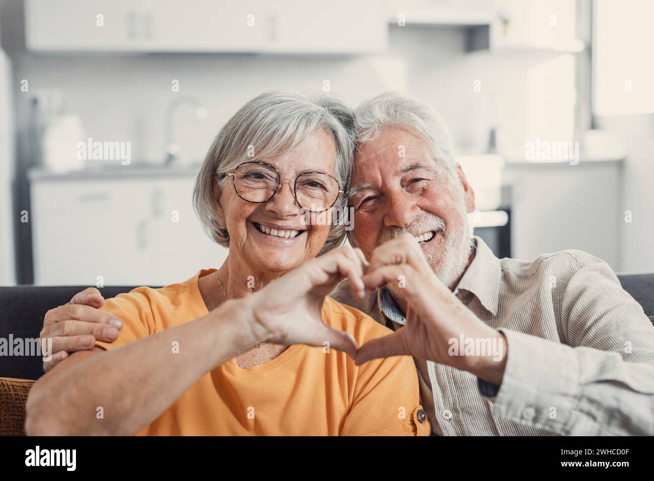 Nahaufnahme Porträt glücklich aufrichtig im mittleren Alter ältere Rentnerfamilie Paar macht Herzgeste mit den Fingern, zeigt Liebe oder zeigt aufrichtige Gefühle zusammen drinnen, Blick auf die Kamera. Stockfoto