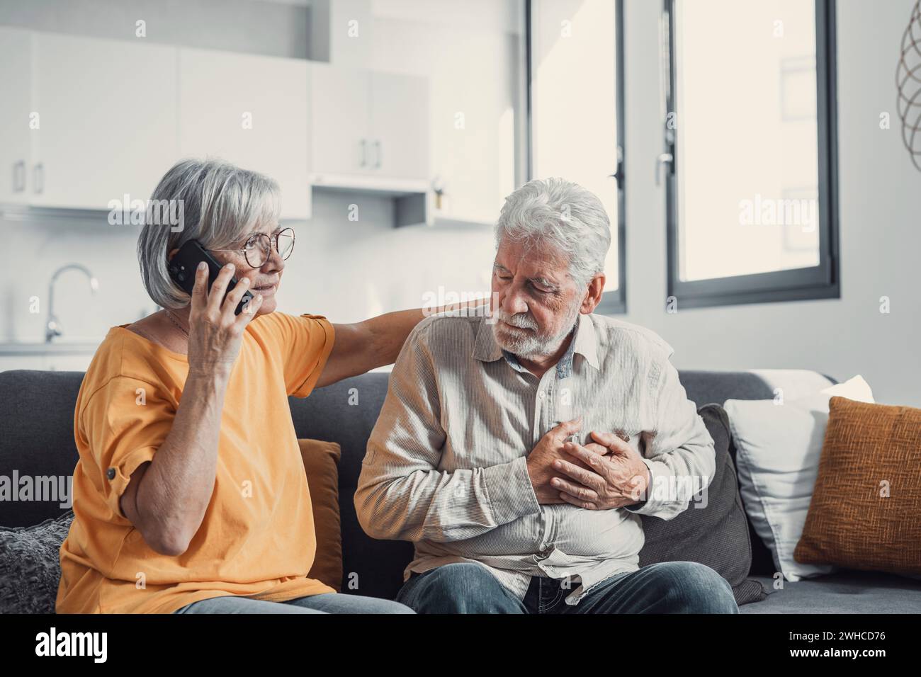 Reife Frau, Ehefrau, die den Notfall ruft, telefoniert, alte Ehemänner Hand hält, grauhaariger Mann hat Herzinfarkt, berührt Brust, leidet an Herzschmerzkrankheit zu Hause, Schmerzen fühlen Stockfoto