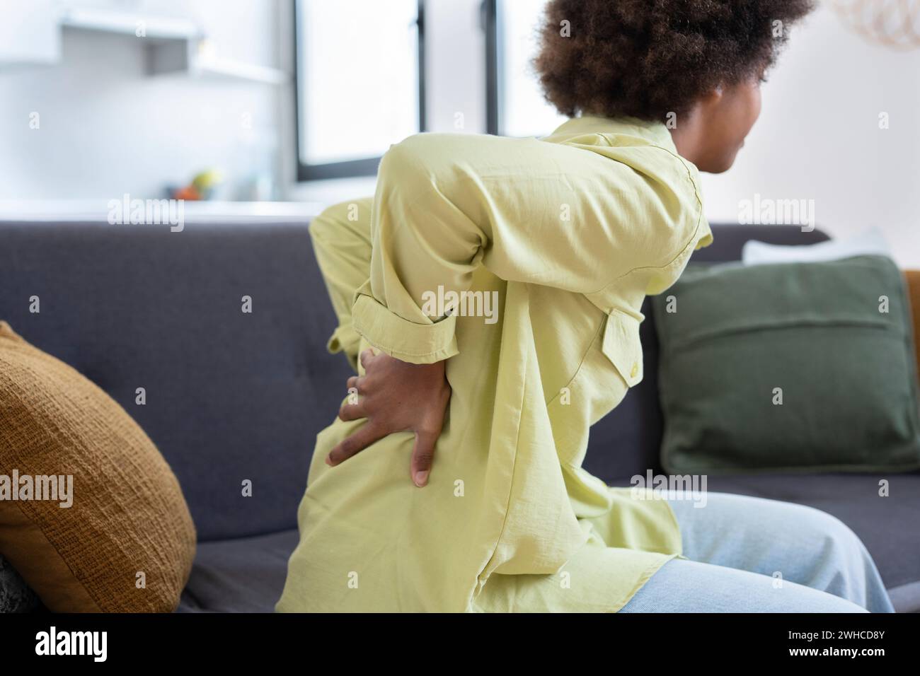 Afro-Studentinnen leiden unter Rückenschmerzen, die sich schlecht fühlen, sitzen auf der Couch im Wohnzimmer zu Hause. Hat Rückenschmerzen, nachdem er lange am Computer studiert hat. Sitzende Arbeit und schlechte Körperhaltung Stockfoto