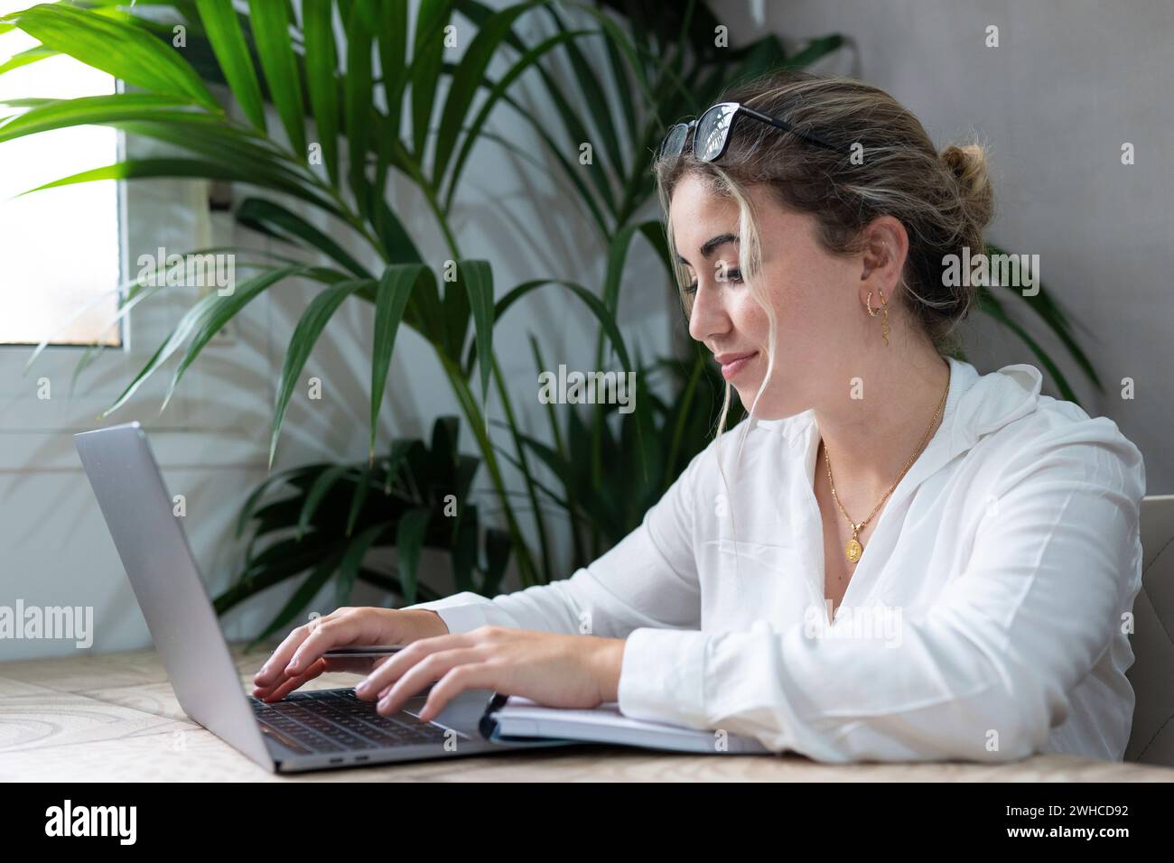 Millennials lächelnde kaukasierin sitzt am Schreibtisch im Wohnzimmer, studiert am Laptop und macht Notizen, konzentriert junge Frau arbeitet am Computer schreibt in Notebook, macht Online-Kurse oder Schulungen zu Hause, Bildungskonzept Stockfoto