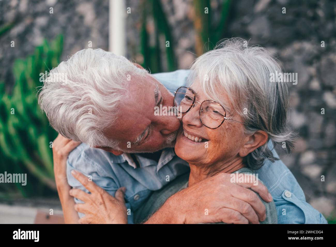 Eine Frau im mittleren Alter sitzt auf der Parkbank und der alte Mann umarmt sie von hinten. Ein paar Rentner entspannen und genießen gemeinsam den Sonnenuntergang im Freien. Stockfoto