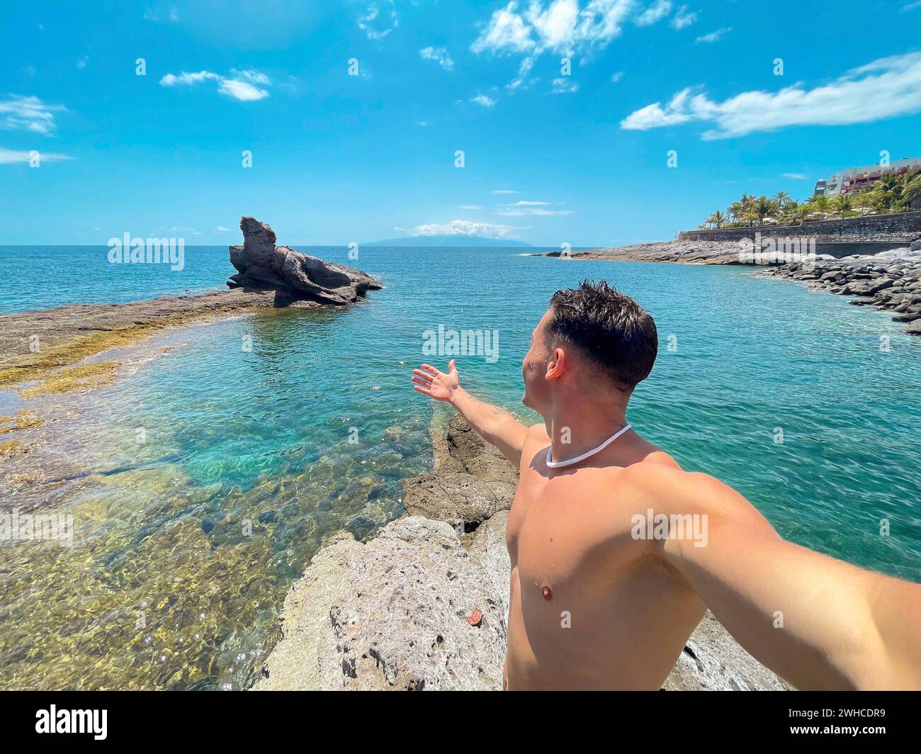 Ein attraktiver und glücklicher junger Mann am Strand, der lächelt und auf das Meer blickt. Die Kamera halten und ein Selfie mit seinem Handy machen. Sommerzeit im Urlaub Spaß und Genießen Stockfoto