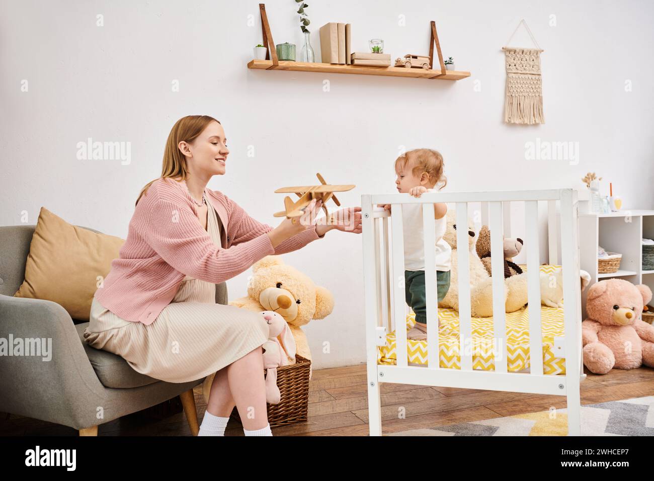 Fröhliche schwangere Frau, die Spielzeugflugzeug in der Nähe des süßen Kleinkindsohnes im Kinderzimmer zu Hause hält, Mutterschaft Stockfoto