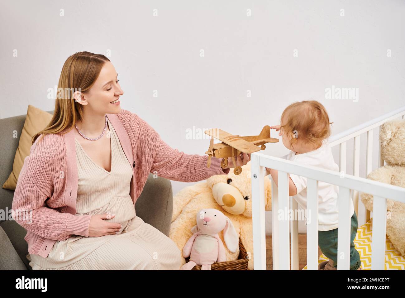 Fröhliche schwangere Frau, die mit Spielzeugflugzeug und Kinderzimmer des kleinen Sohnes zu Hause spielt, glückliche Mutterschaft Stockfoto