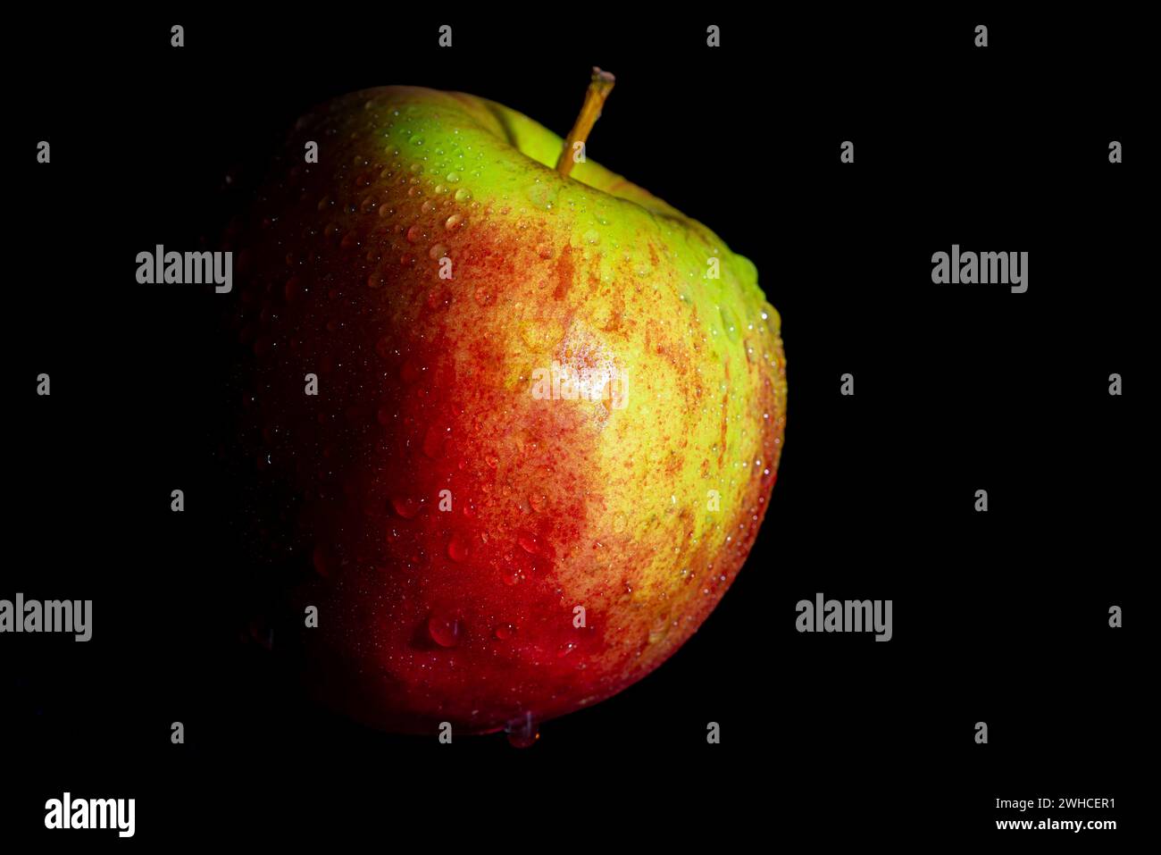 Roter Apfel mit grünen Flecken und Wassertröpfchen, dunkler Hintergrund Stockfoto