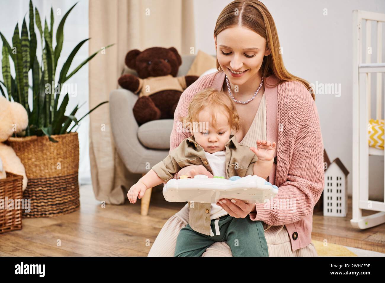 Lächelnde Mutter, die mit einem entzückenden Kleinkind auf dem Boden im Kinderzimmer spielt, glückselige Mutterschaft Stockfoto