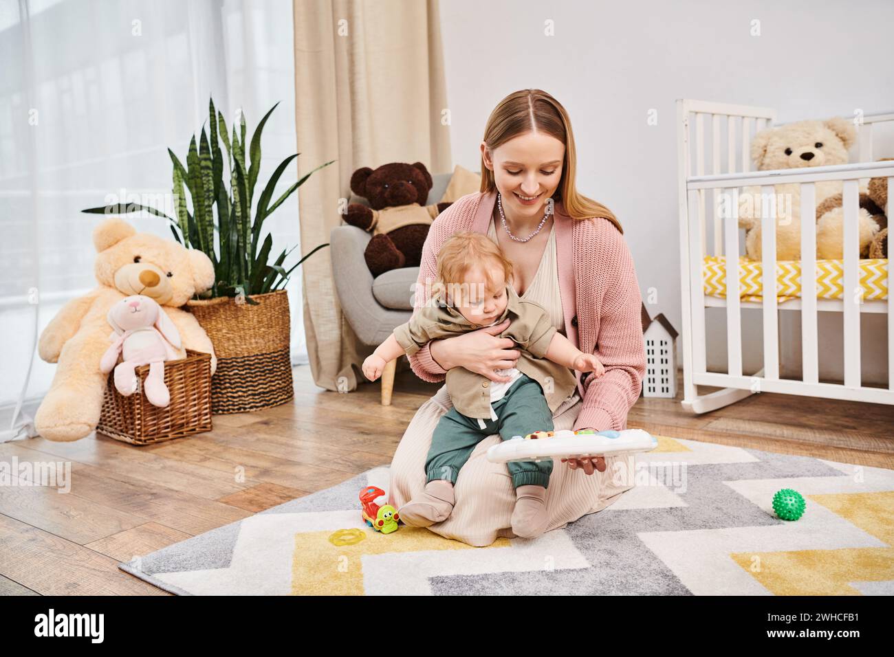 Junge, fröhliche Frau, die mit dem süßen Kleinkind-Sohn auf dem Boden im Kinderzimmer spielt, glückselige Mutterschaft Stockfoto