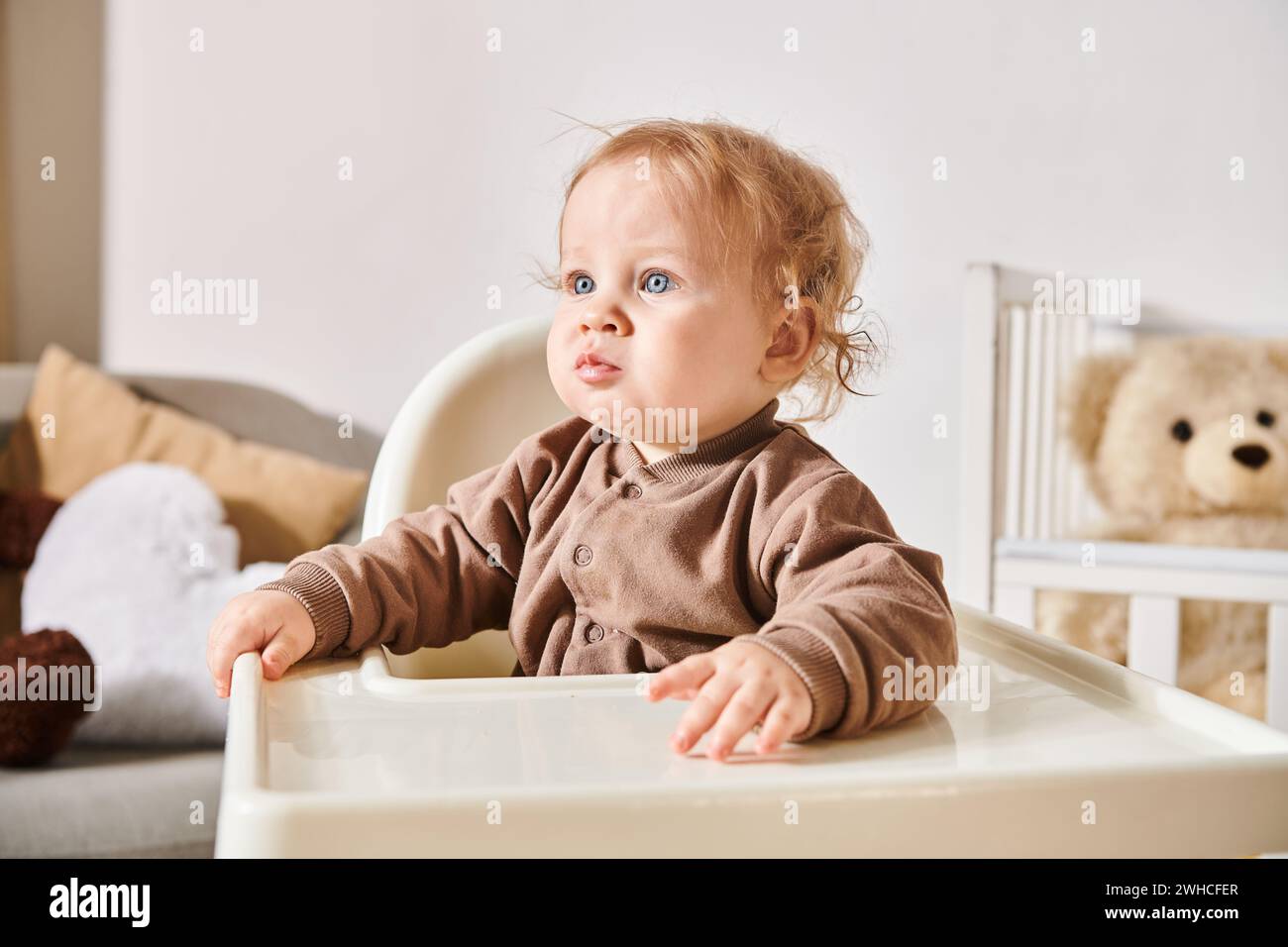 Porträt eines kleinen Kleinkindes, der im Kinderstuhl sitzt und zu Hause im Kinderzimmer wegschaut Stockfoto