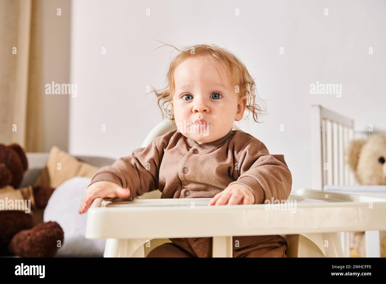 Porträt eines niedlichen Kleinkindes, der im Kinderstuhl sitzt und die Kamera im Kinderzimmer zu Hause betrachtet Stockfoto
