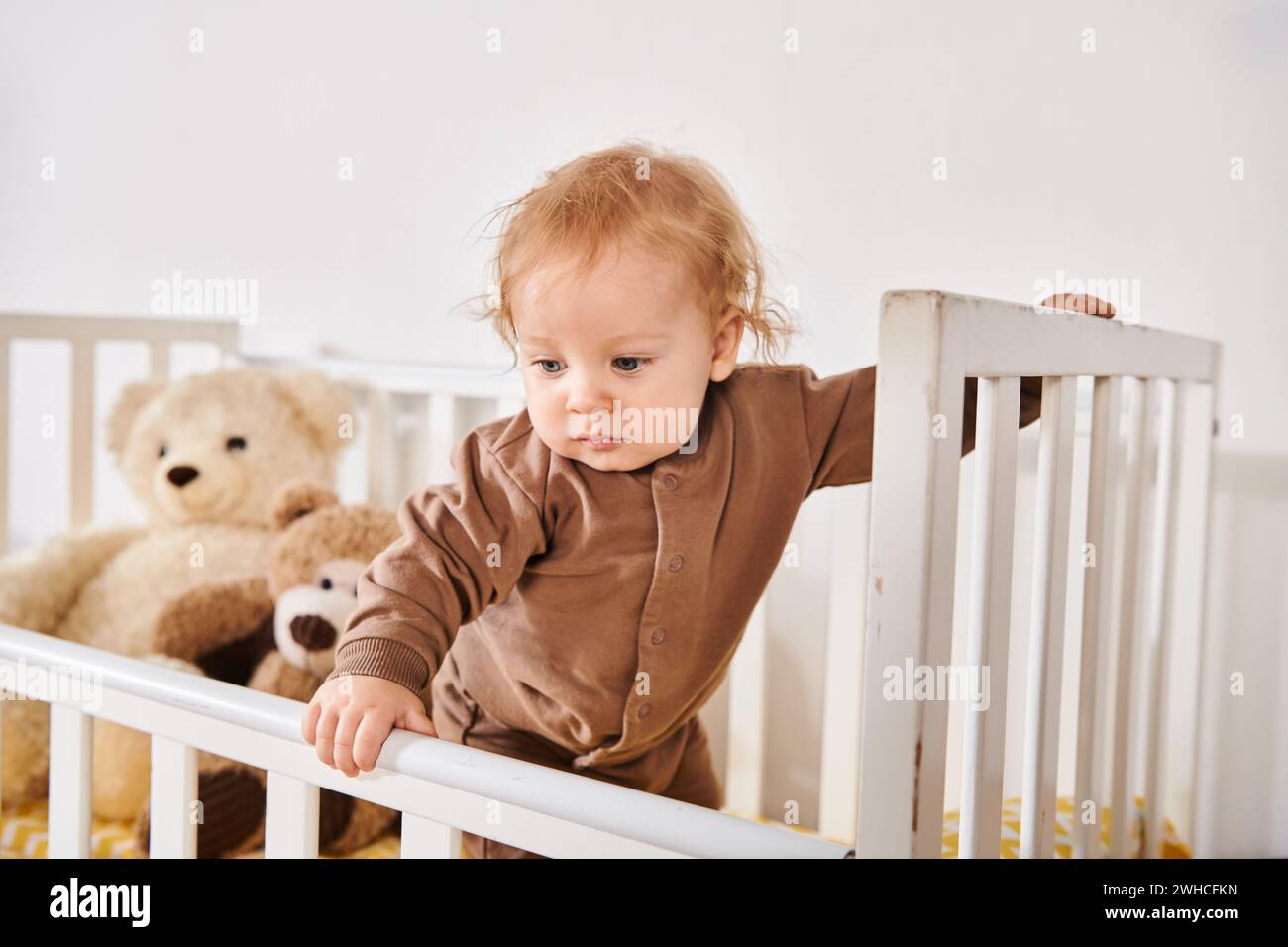 Glückliche Kindheit, entzückender kleiner Junge, der im Kinderbett mit weichen Spielzeugen im gemütlichen Kinderzimmer zu Hause steht Stockfoto
