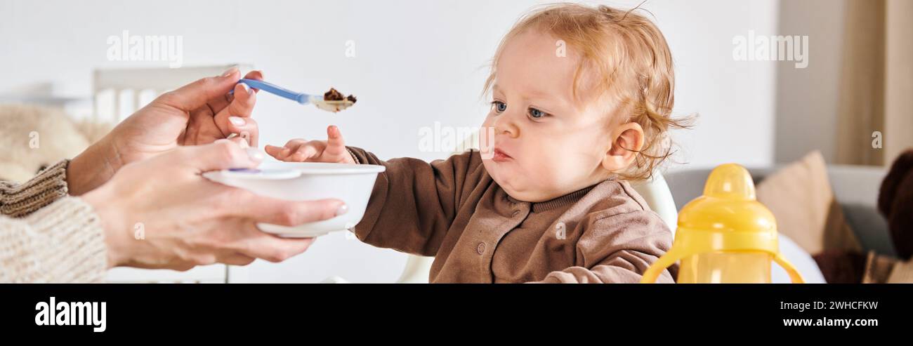 Junge Frau füttert ein kleines Kind mit Frühstück auf Kinderstuhl im Kinderzimmer, horizontales Banner Stockfoto