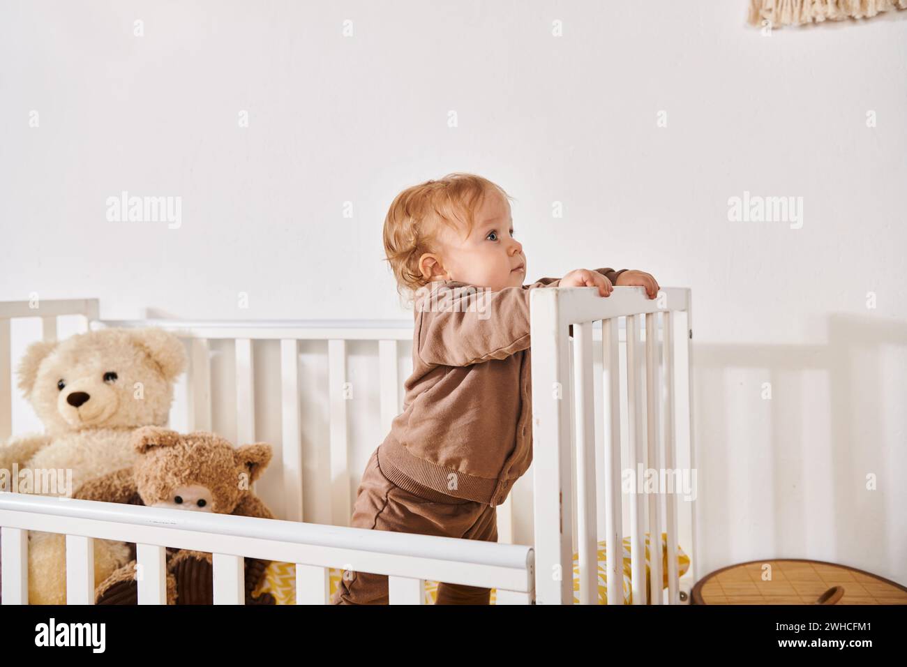 Neugieriger Junge, der in der Krippe mit Kuschelspielzeug im gemütlichen Kinderzimmer zu Hause steht, glückselige Kindheit Stockfoto