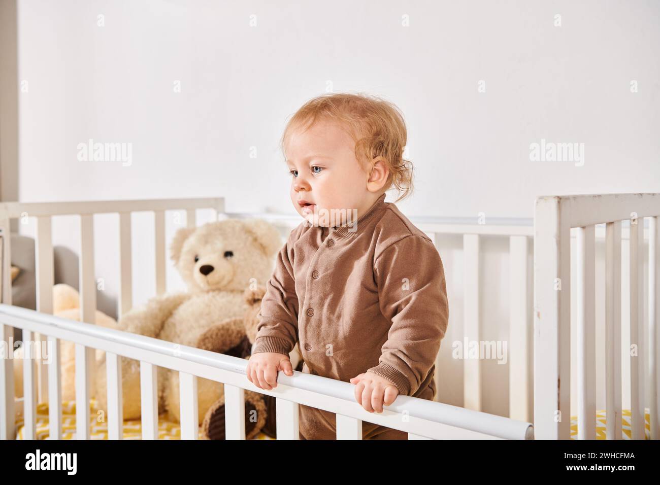 Glückliche Kindheit, entzückender kleiner Junge, der im Kinderbett mit weichen Spielzeugen im gemütlichen Kinderzimmer zu Hause steht Stockfoto