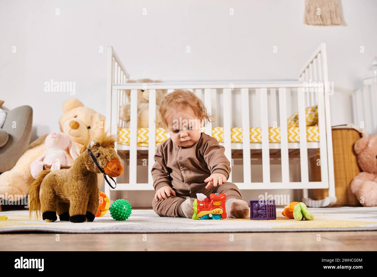 Niedliches Kleinkind, das auf dem Boden sitzt und mit Spielzeug im gemütlichen Kinderzimmer spielt, glückliche Kindheit Stockfoto