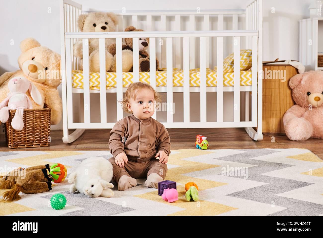 Kleiner Junge, der auf dem Boden in der Nähe von Kuschelspielzeug und Kinderbett im gemütlichen Kinderzimmer sitzt, glückliches Kleinkind Stockfoto