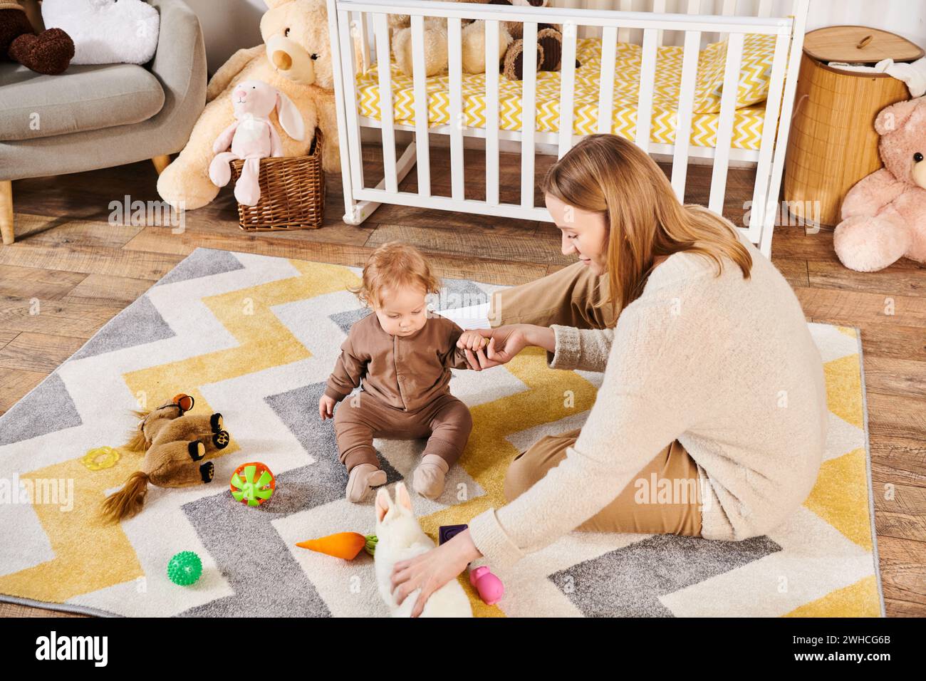 Fröhliche Mutter und Sohn des Kleinkindes spielen mit weichen Spielzeugen in der Nähe des Kinderzimmers, moderne Eltern Stockfoto