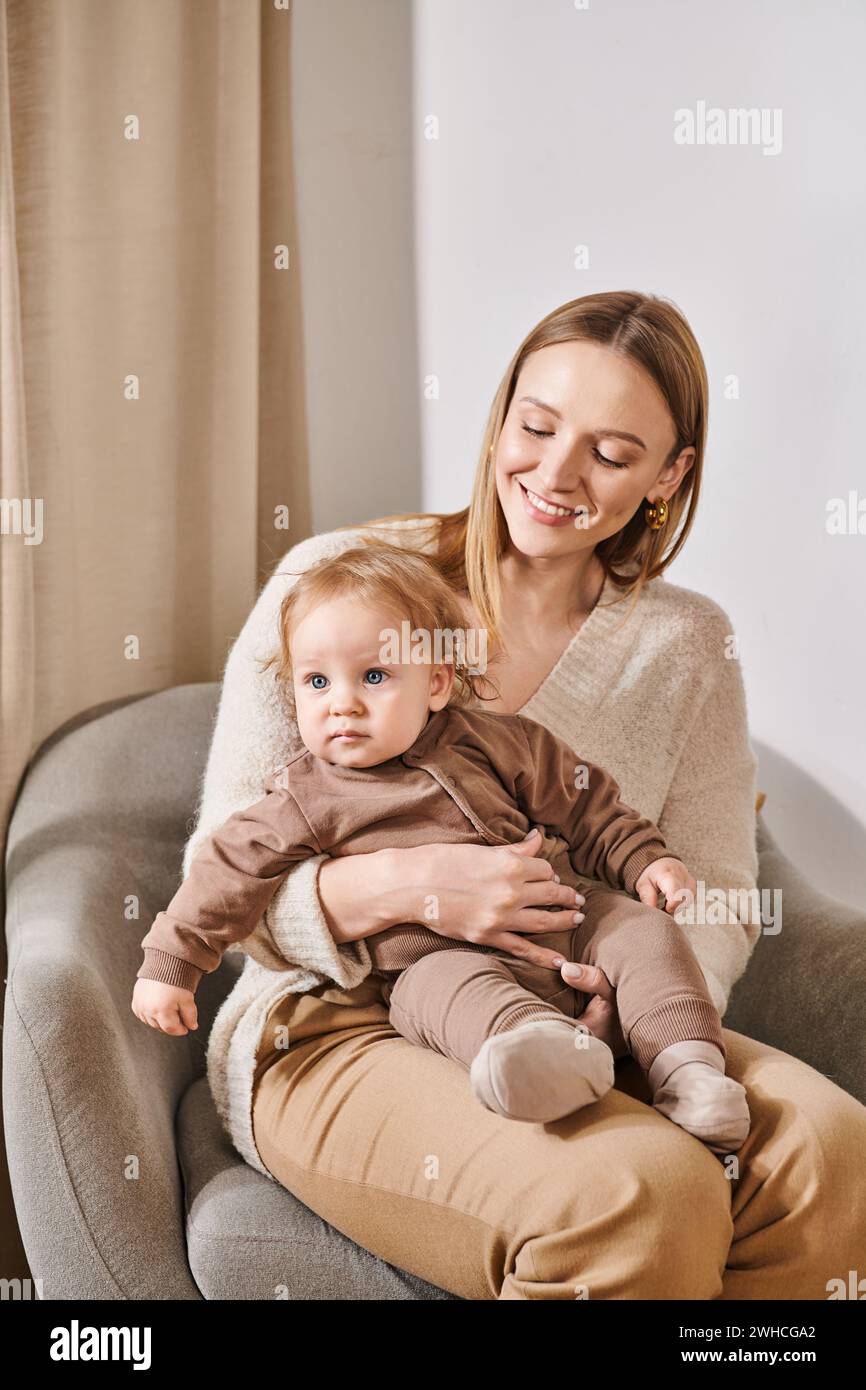 Fröhliche attraktive Frau, die im Sessel mit einem kleinen Jungen im gemütlichen Kinderzimmer sitzt, Mutter und Sohn Stockfoto