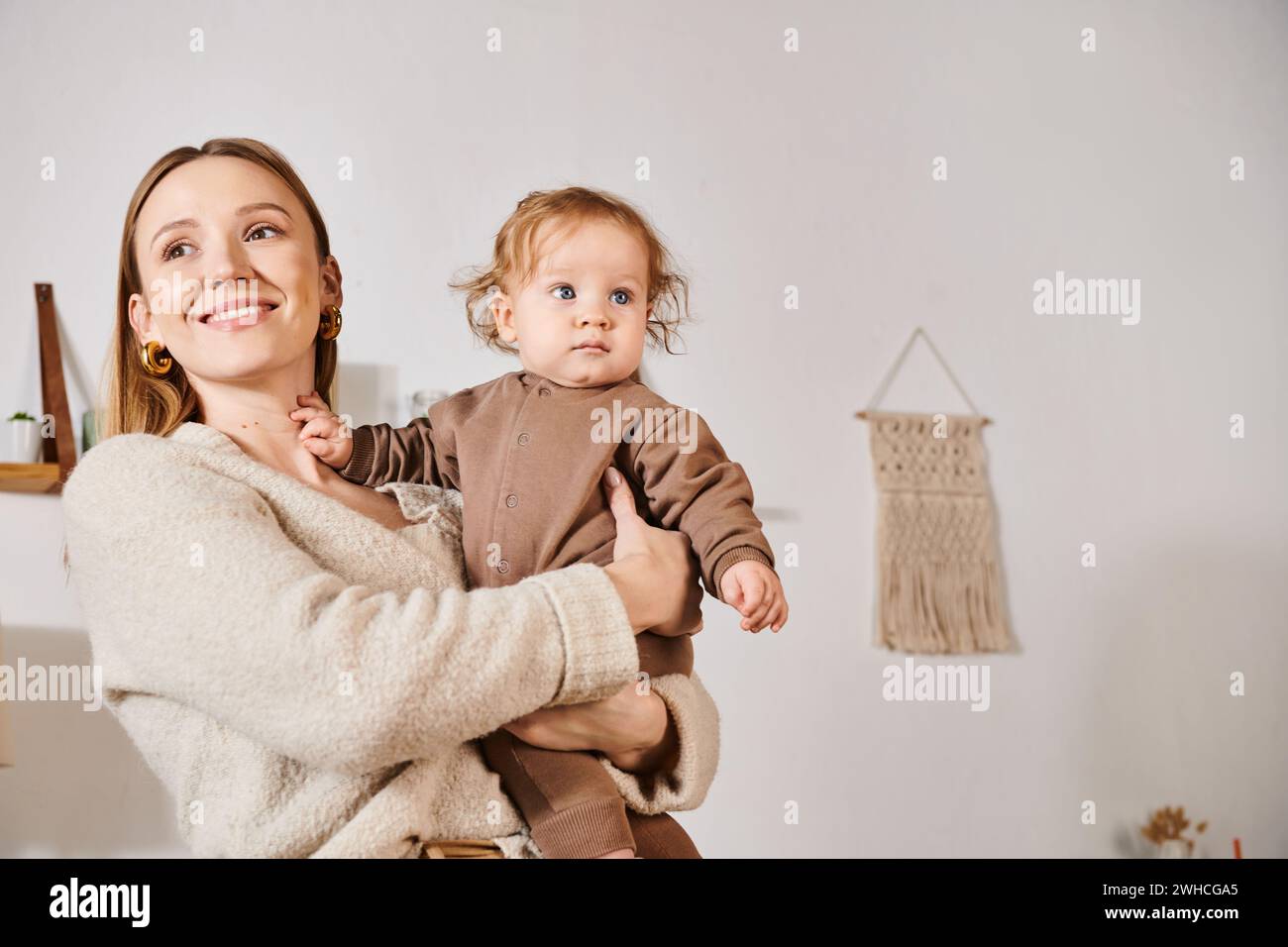 Fröhlich lächelnde Frau, die den Jungen in einem gemütlichen Kinderzimmer hält und umschließt, glückselige Mutterschaft Stockfoto