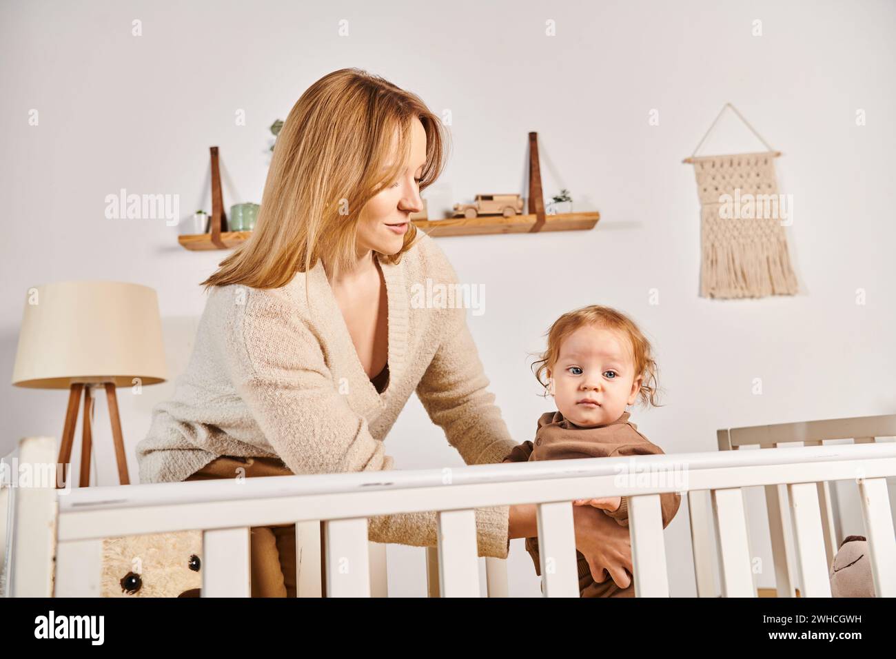 Glückliche junge Mutter, die ein kleines Kind unterstützt, das im Kinderzimmer zu Hause steht, Mutterschaft Stockfoto