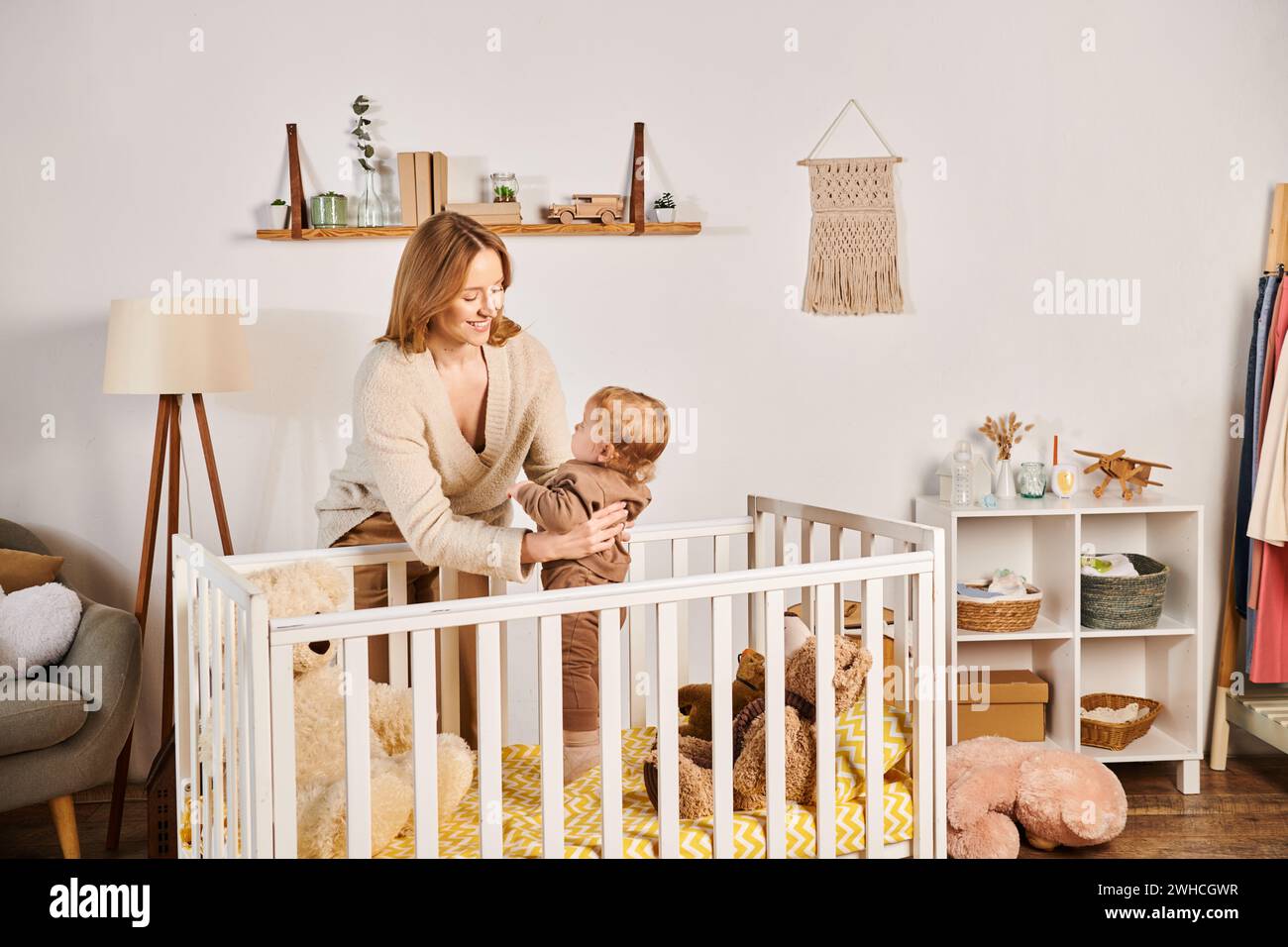 Fröhliche junge Mutter, die den süßen Kleinkind-Sohn in der Nähe des Kinderzimmers hält, glückselige Mutterschaft Stockfoto