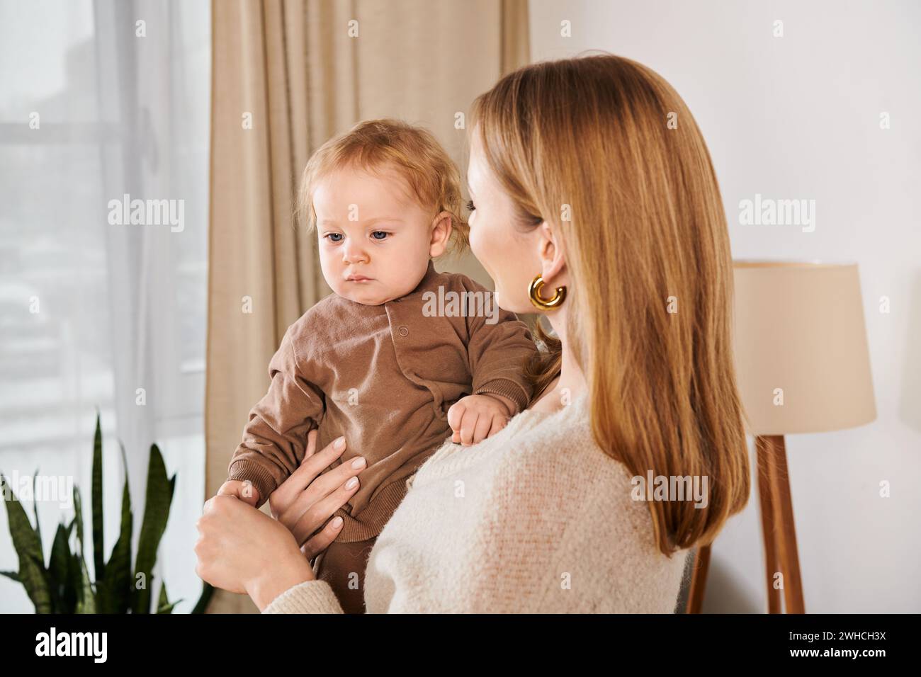 Glückliche Mutter, die den entzückenden kleinen Sohn in den Händen hält, im Kinderzimmer zu Hause, moderne Mutterschaft Stockfoto
