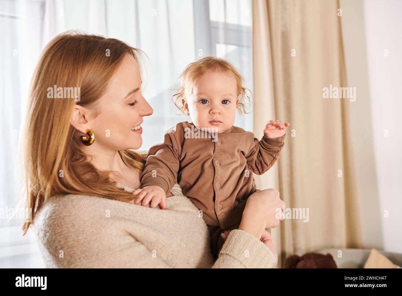 Fröhliche Frau, die den kleinen Jungen in den Händen hält, im Kinderzimmer zu Hause, glückselige Mutterschaft Stockfoto