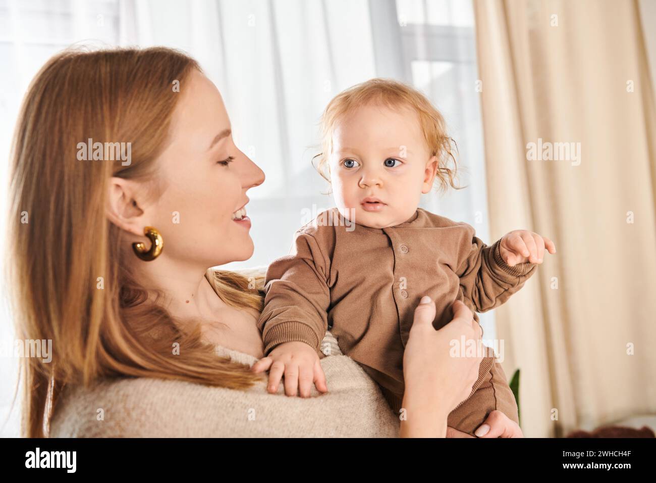 Junge lächelnde Frau, die den kleinen Jungen in der Hand hält, im Kinderzimmer zu Hause, glückliche Mutterschaft Stockfoto