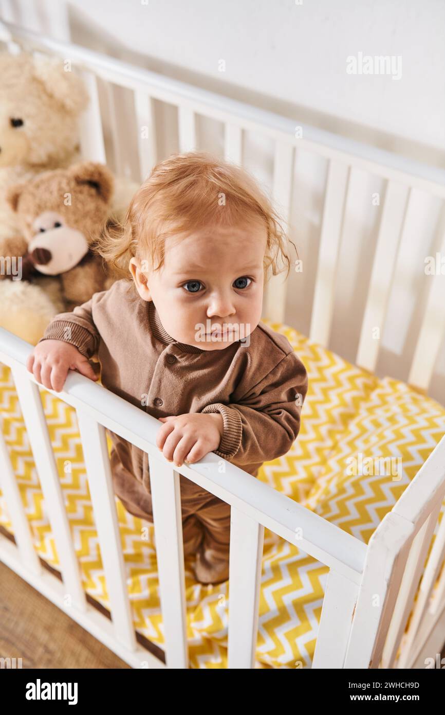 Hochwinkelansicht des Kleinkindes im Strampler stehend in einem gemütlichen Kinderbett im Kinderzimmer zu Hause Stockfoto
