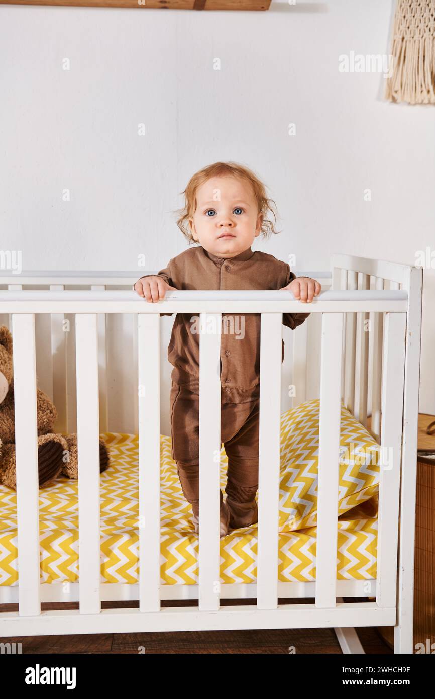 Entzückendes Kleinkind Baby Boy im Strampler stehend in der Krippe im Kinderzimmer zu Hause, glückliche Kindheit Stockfoto