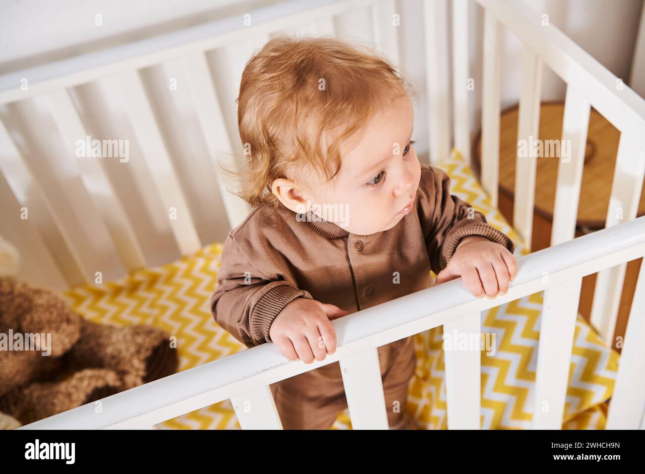 Blick aus der Höhe auf den niedlichen kleinen Jungen im Strampler, der im Kinderzimmer zu Hause steht, Kleinkind Stockfoto
