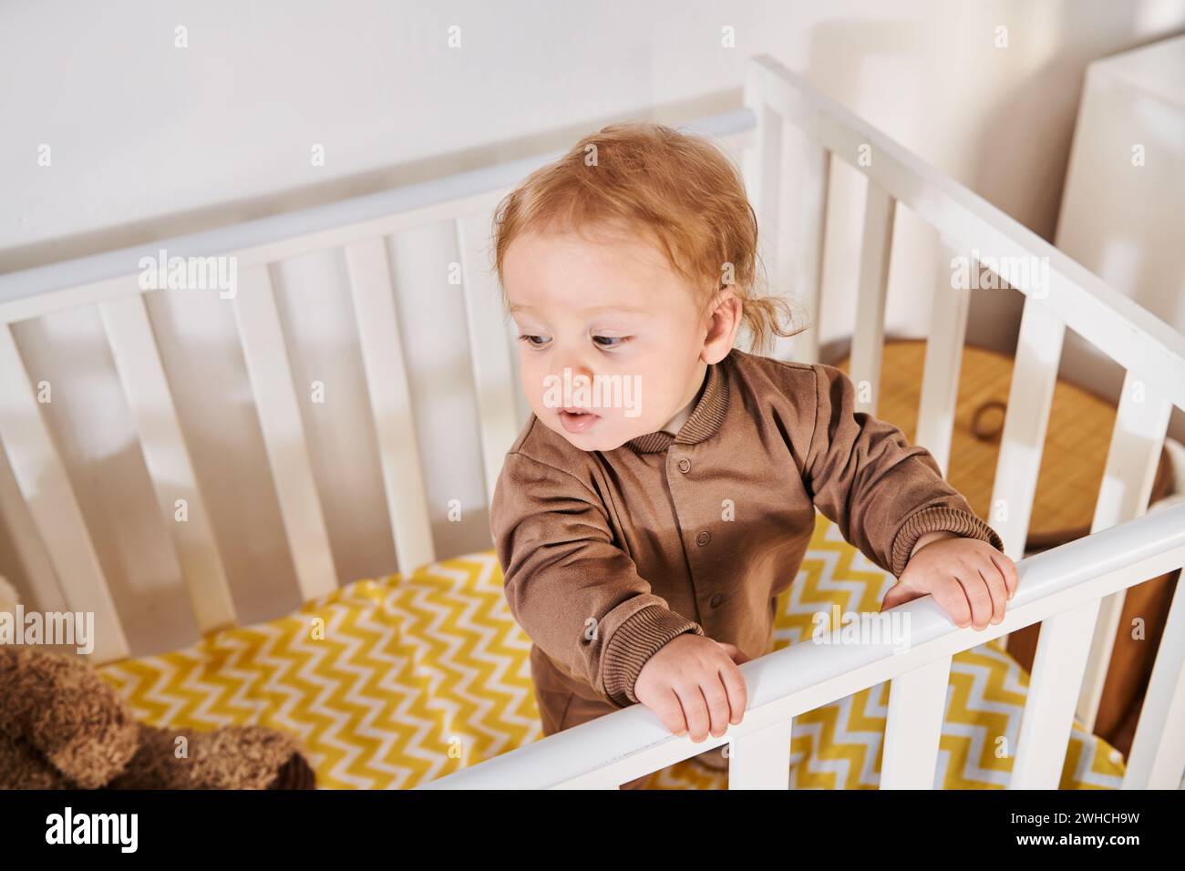 Hochwinkelansicht des liebenswerten Kindes im Strampler, das im Kinderzimmer zu Hause steht, Kleinkind Stockfoto