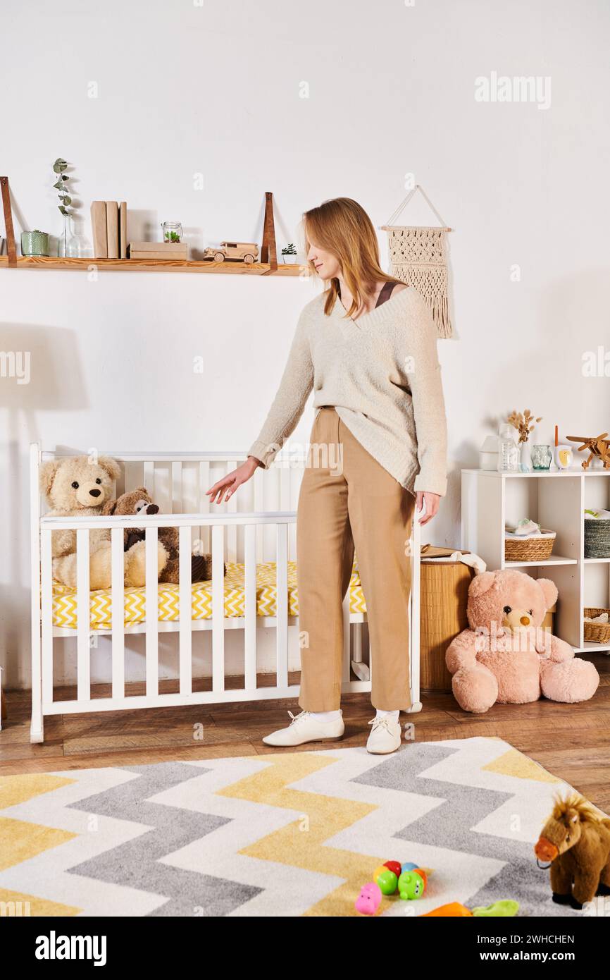 Junge schwangere Frau, die in der Nähe einer Krippe im Kinderzimmer steht, mit Kuschelspielzeug zu Hause, Geburtserwartung Stockfoto