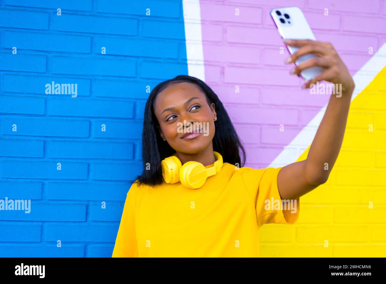 Frontales Nahporträt einer afrikanerin, die lächelnd ein Selfie gegen eine bunte Wand macht Stockfoto