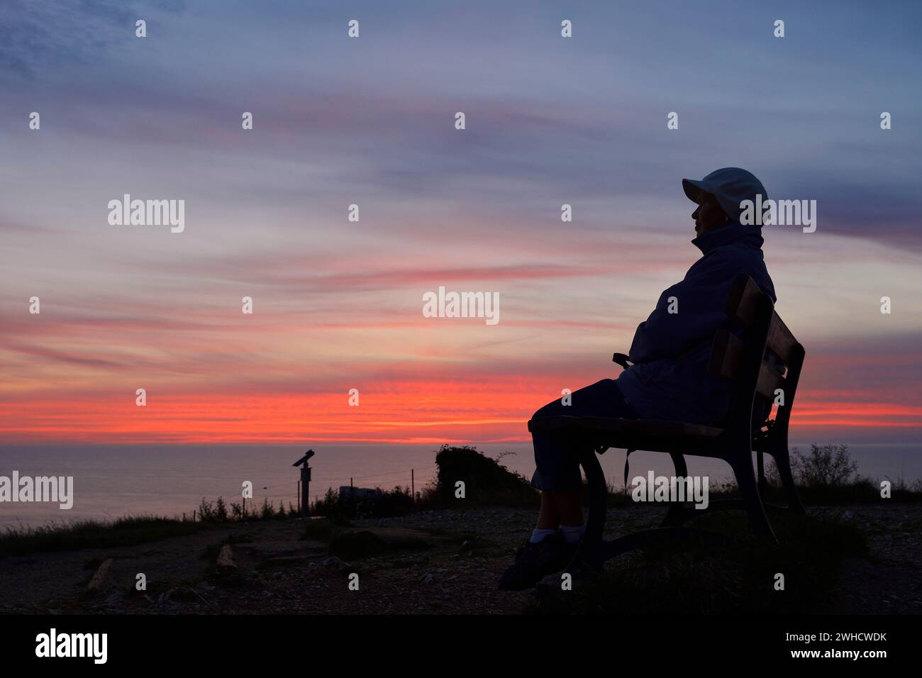 Frau, die in der Abenddämmerung auf einer Bank auf den Klippen sitzt, Etretat, seine-Maritime, Normandie, Frankreich Stockfoto