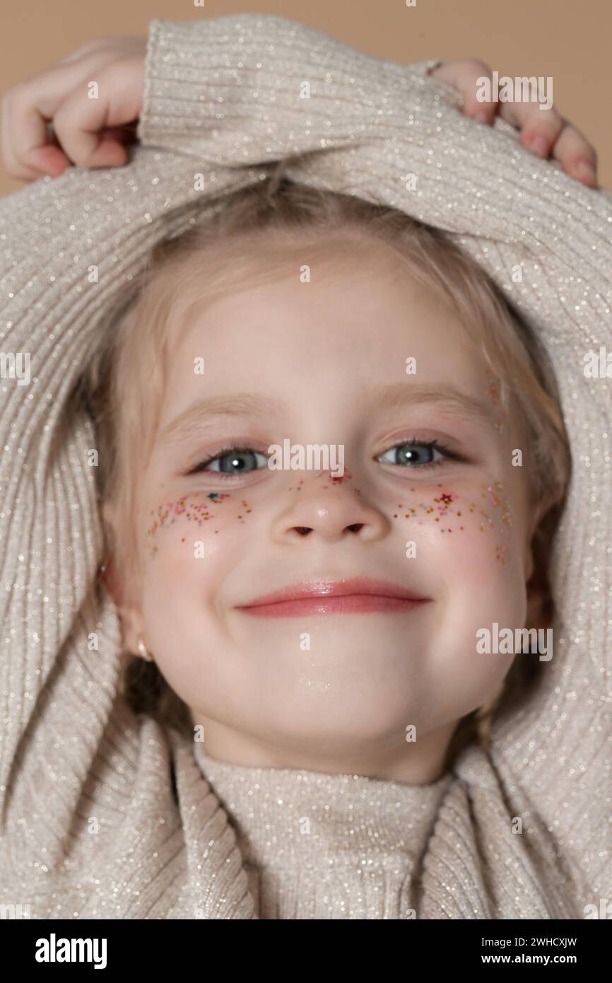 Porträt eines süßen kleinen blonden Mädchens mit blauen Augen und Glitzern im Gesicht. Stockfoto