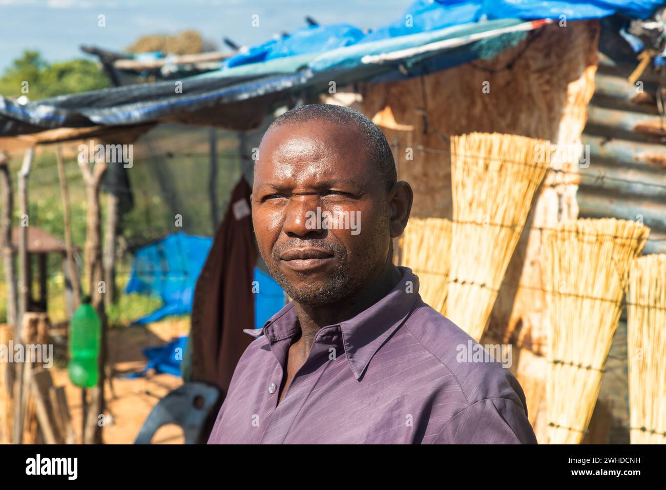 afrikanisches Dorf, Straßenverkäufer, alter Unternehmer, der Besen verkauft, kleines Geschäft Stockfoto