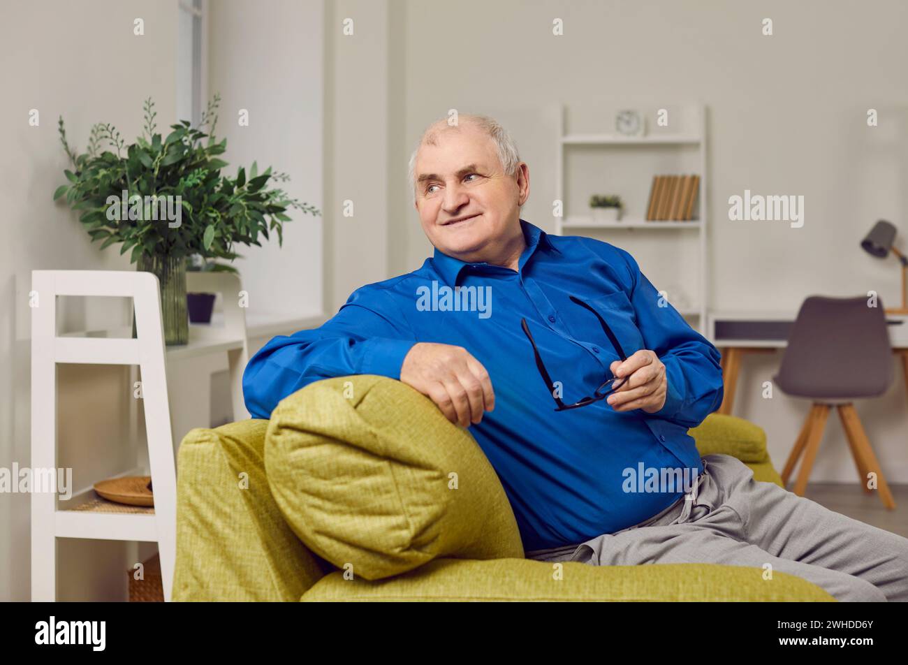 Porträt eines alten Mannes im Ruhestand mit grauen Haaren, der auf dem Sofa sitzt Stockfoto