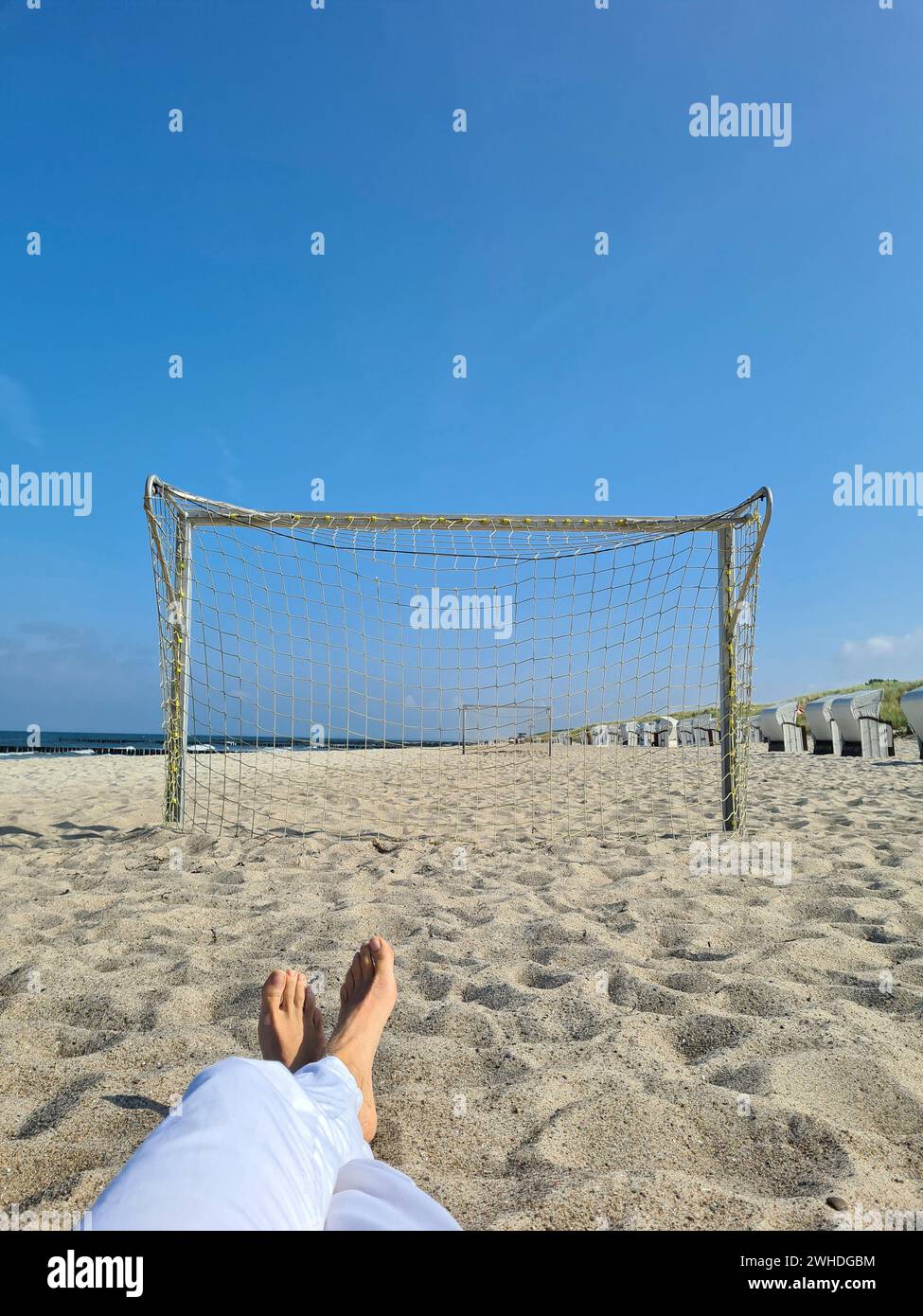 Frauenfüße entspannen in der Sonne am Meer, Blick durch das Fußballtor am Strand von Markgrafenheide, Ostsee, Deutschland Stockfoto