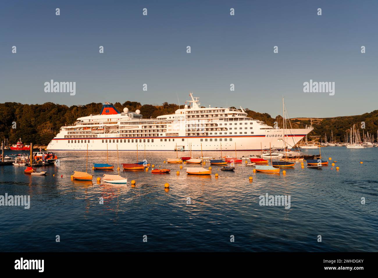 Das Kreuzfahrtschiff Europa liegt an einem Sommerabend im Hafen von Fowey Bay in Cornwall, umgeben von kleinen Booten Stockfoto