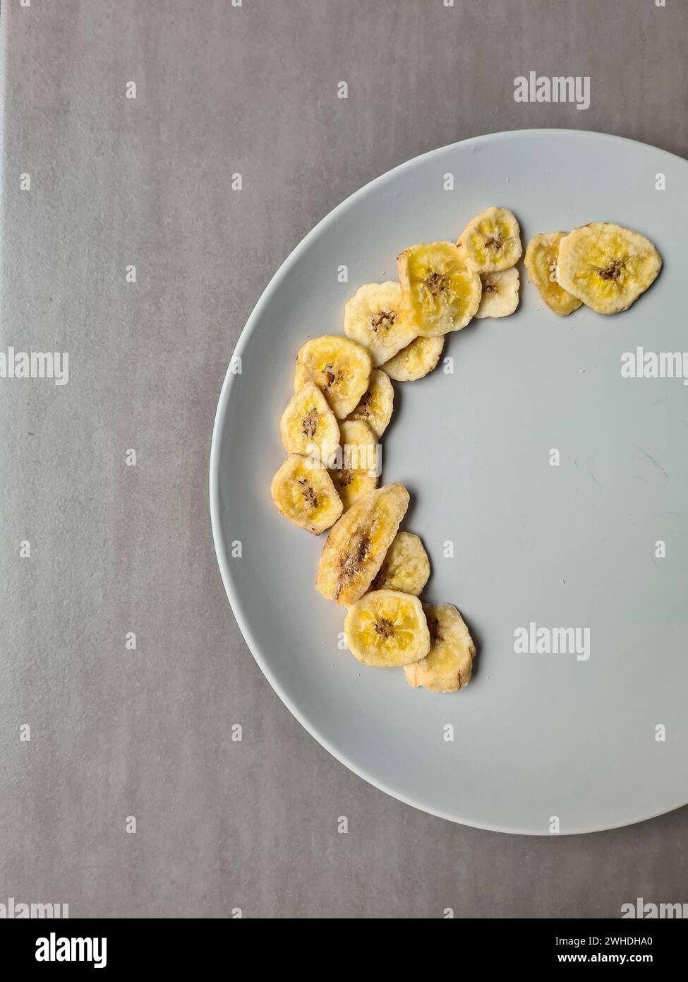 Bananenchips auf einem hellgrauen Teller als Nachtisch und Snack zwischen den Mahlzeiten Stockfoto