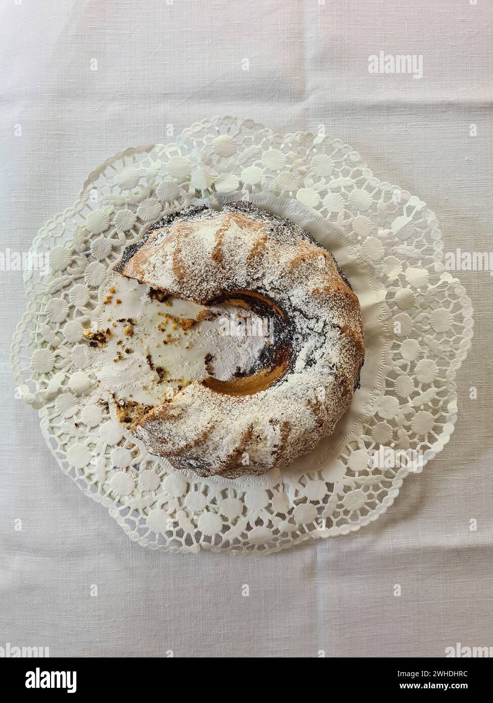 Der runde Marmorkuchen mit weißem Puderzucker wird auf der linken Seite geschnitten und ein Viertel des Kuchens fehlt auf dem Teller Stockfoto