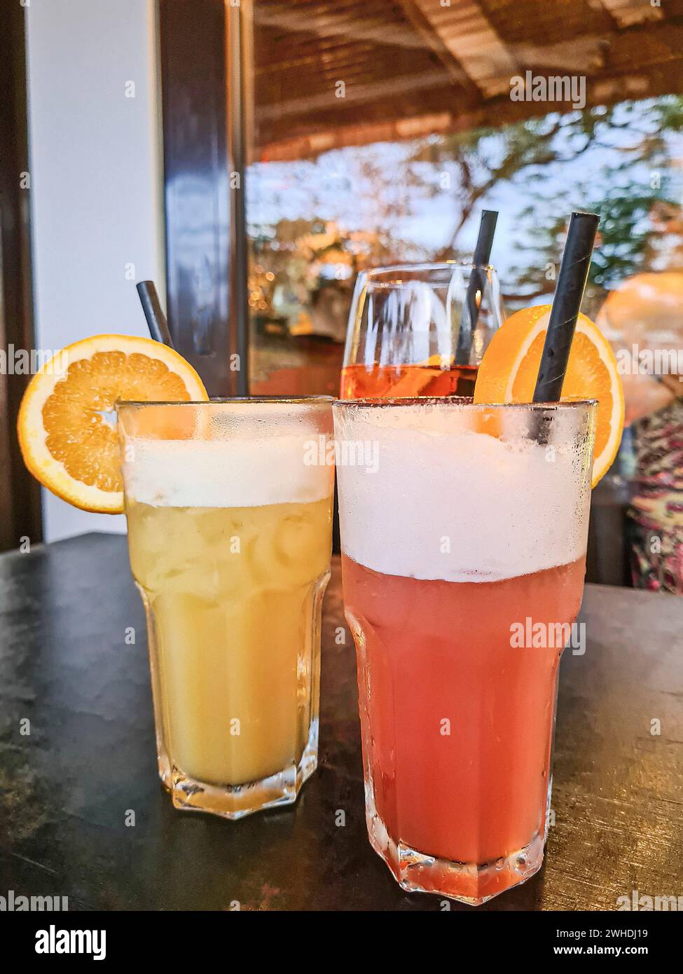 Zwei alkoholfreie Cocktails in einem Glas mit Orangenscheibe und Strohhalm stehen im Vordergrund auf einem Tisch Stockfoto