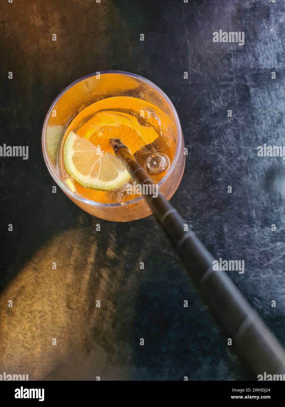 Ein orangenfarbenes Sommergetränk mit Alkohol in einem Glas mit schwarzem Strohhalm und einer Zitronenscheibe im Restaurant Stockfoto