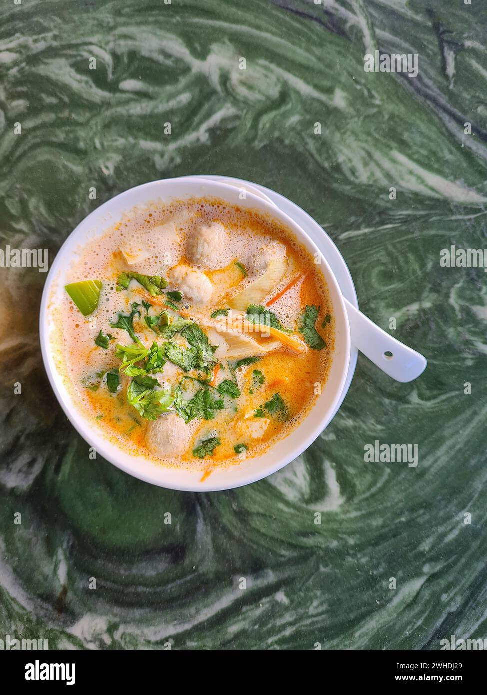 Tom Kha Gai, Hühnersuppe in einer weißen Schüssel, enthält die Zutaten Kokosmilch, Galgant, Zitronengras, Hühnchen, Lauch und Petersilie Stockfoto